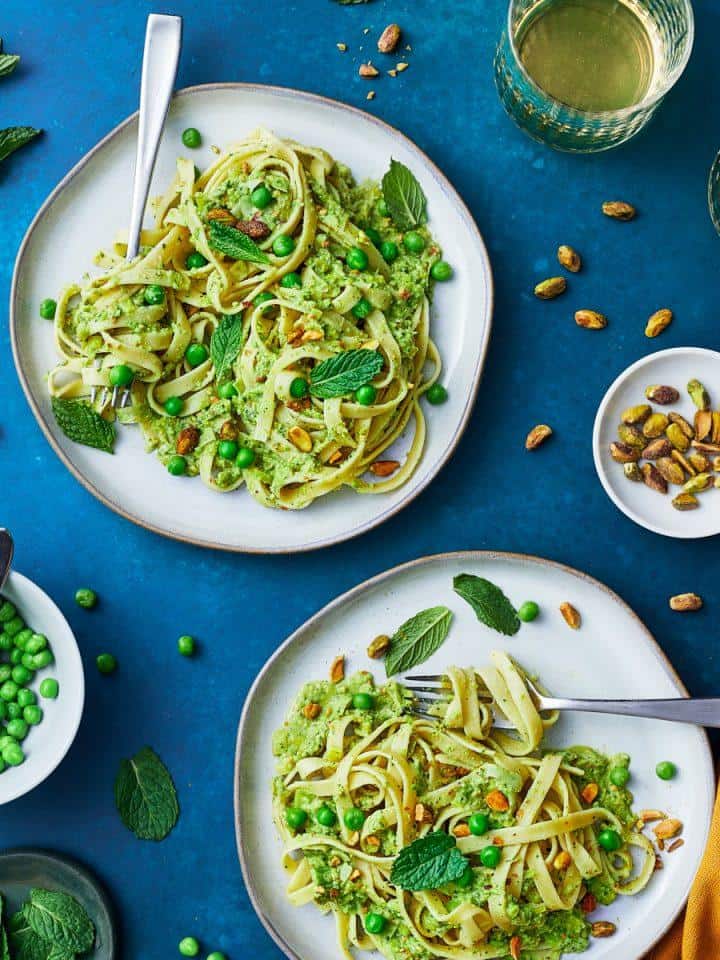 two plates of pasta with peas and mint pesto with a side of peas and drink glasses