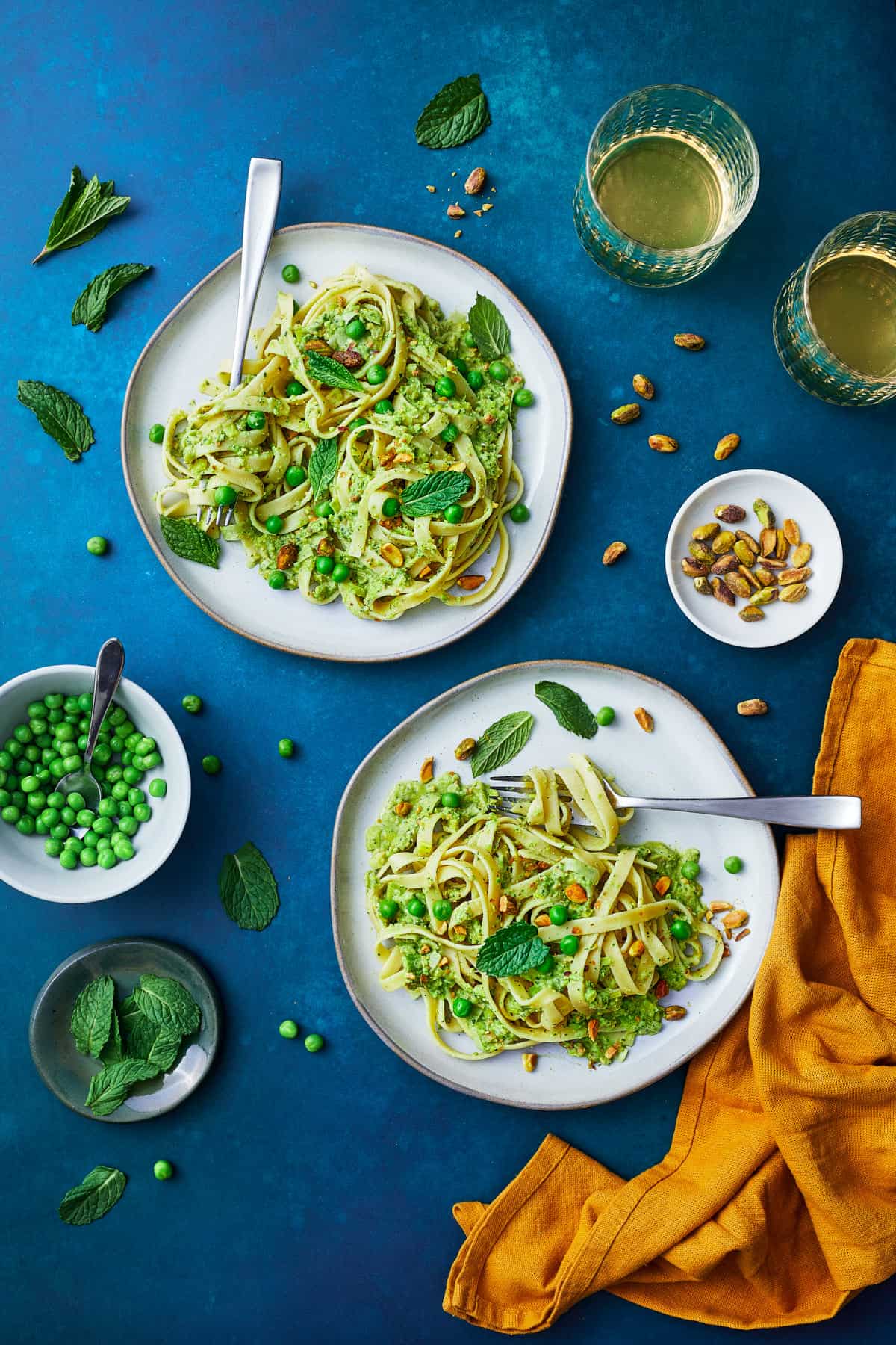 plates of green pea pasta with pesto, mint leaves and white wine glasses