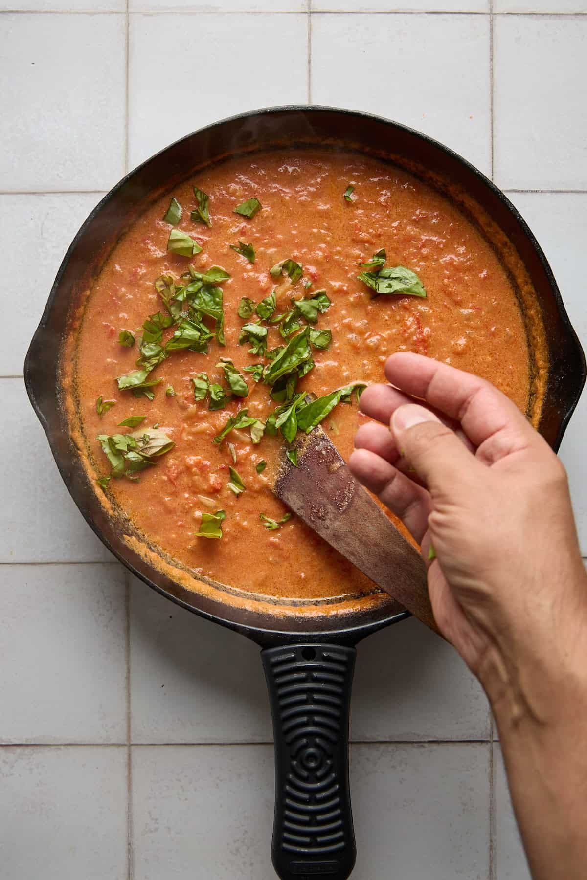 chopped basil being added to pan of creamy rum pasta sauce
