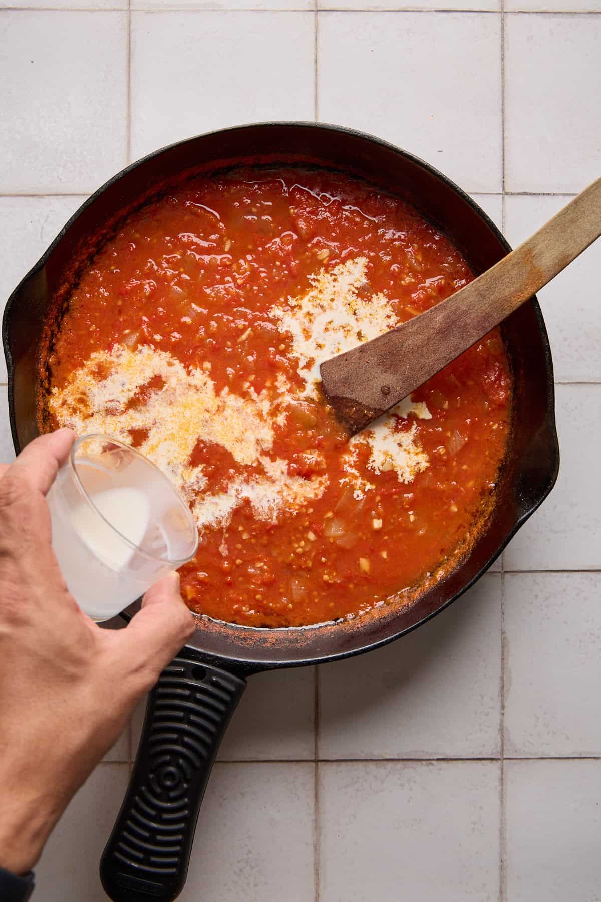 cream being poured into rum tomato sauce