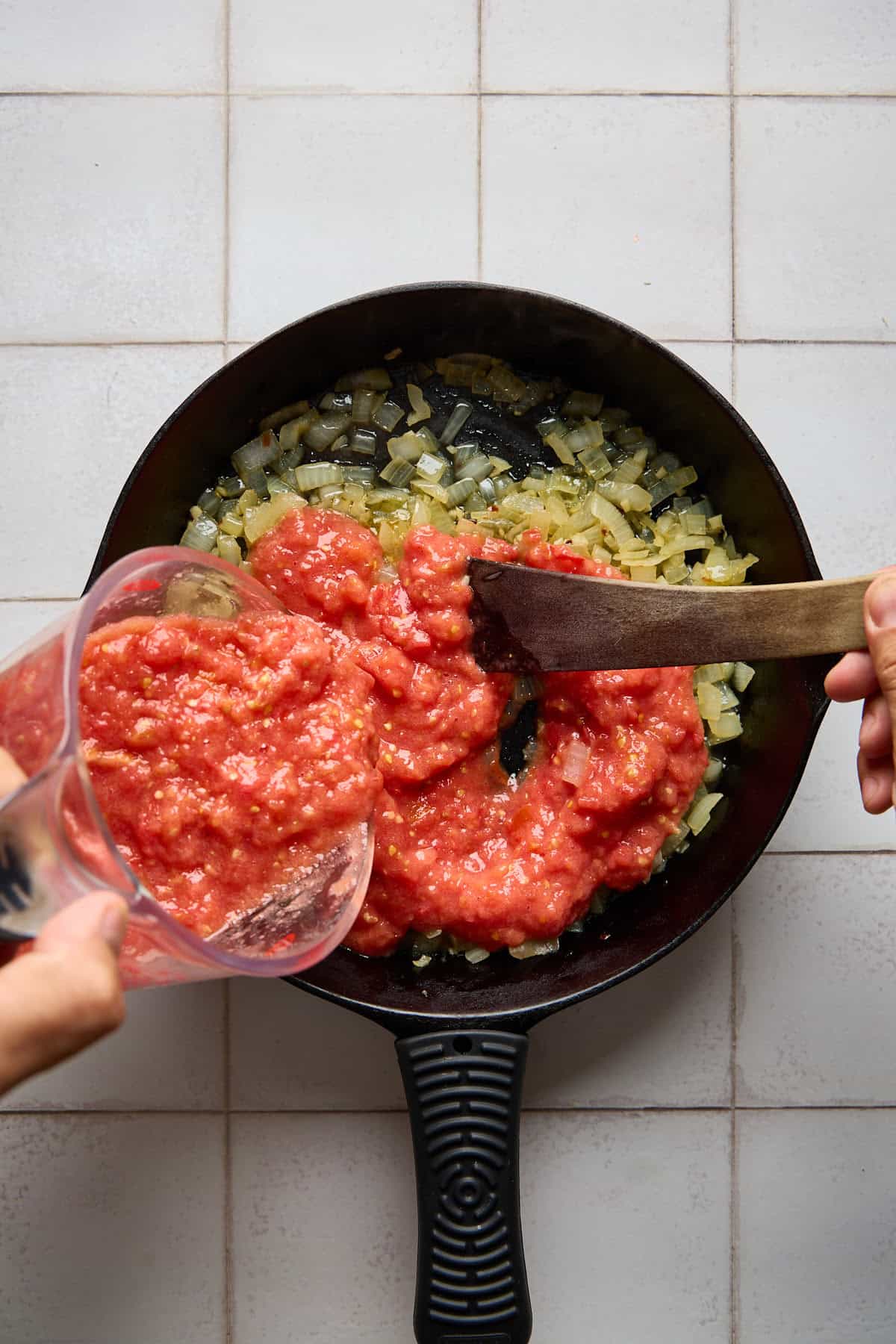 crushed tomatoes being poured into pan with onions