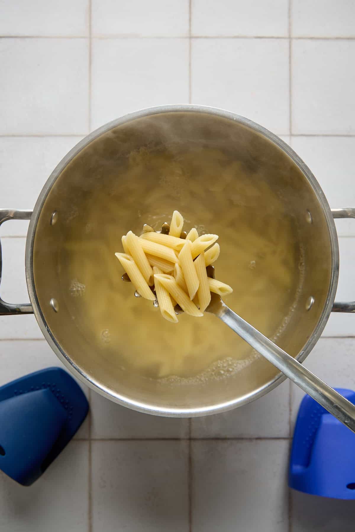 penne in a spoon over a pot of boiling pasta