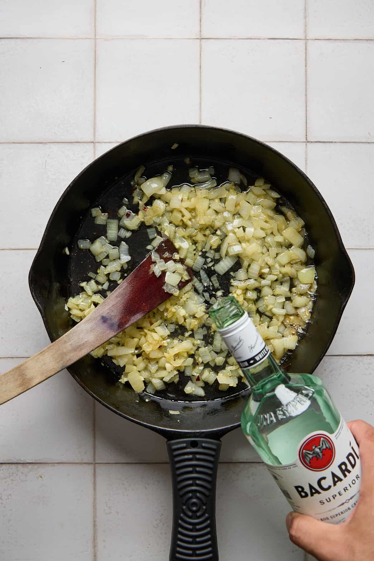 white rum being poured into pan with onions