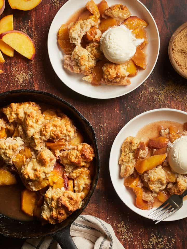 peach cobbler in a cast iron pan with two plates and sliced peaches
