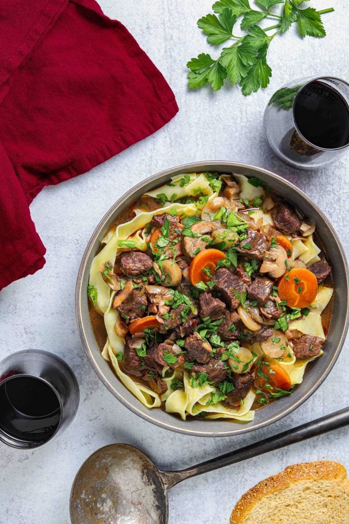 red wine beef stew in plate over noodles with wine