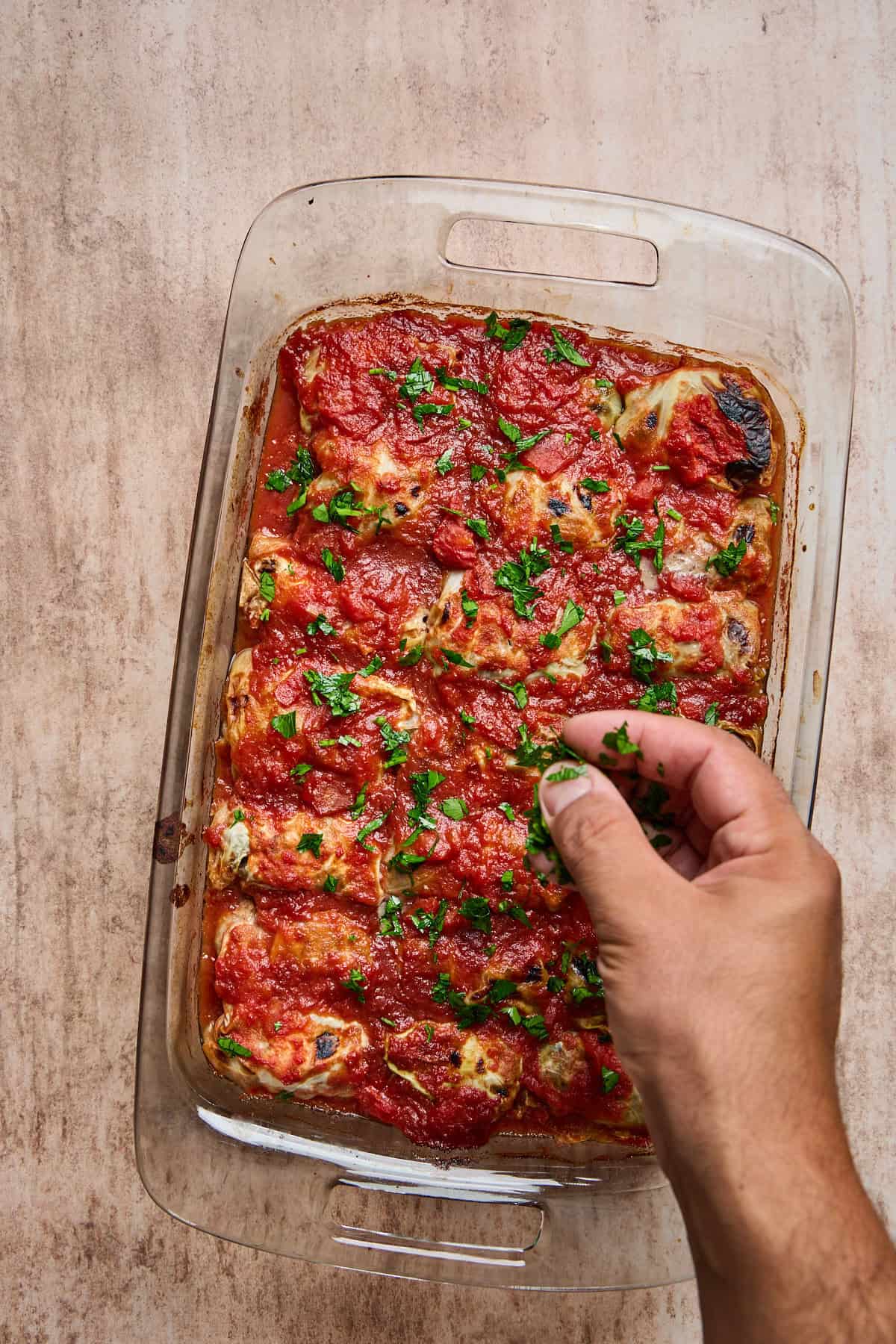 parsley being sprinkled over a pan of baked stuffed cabbage rolls