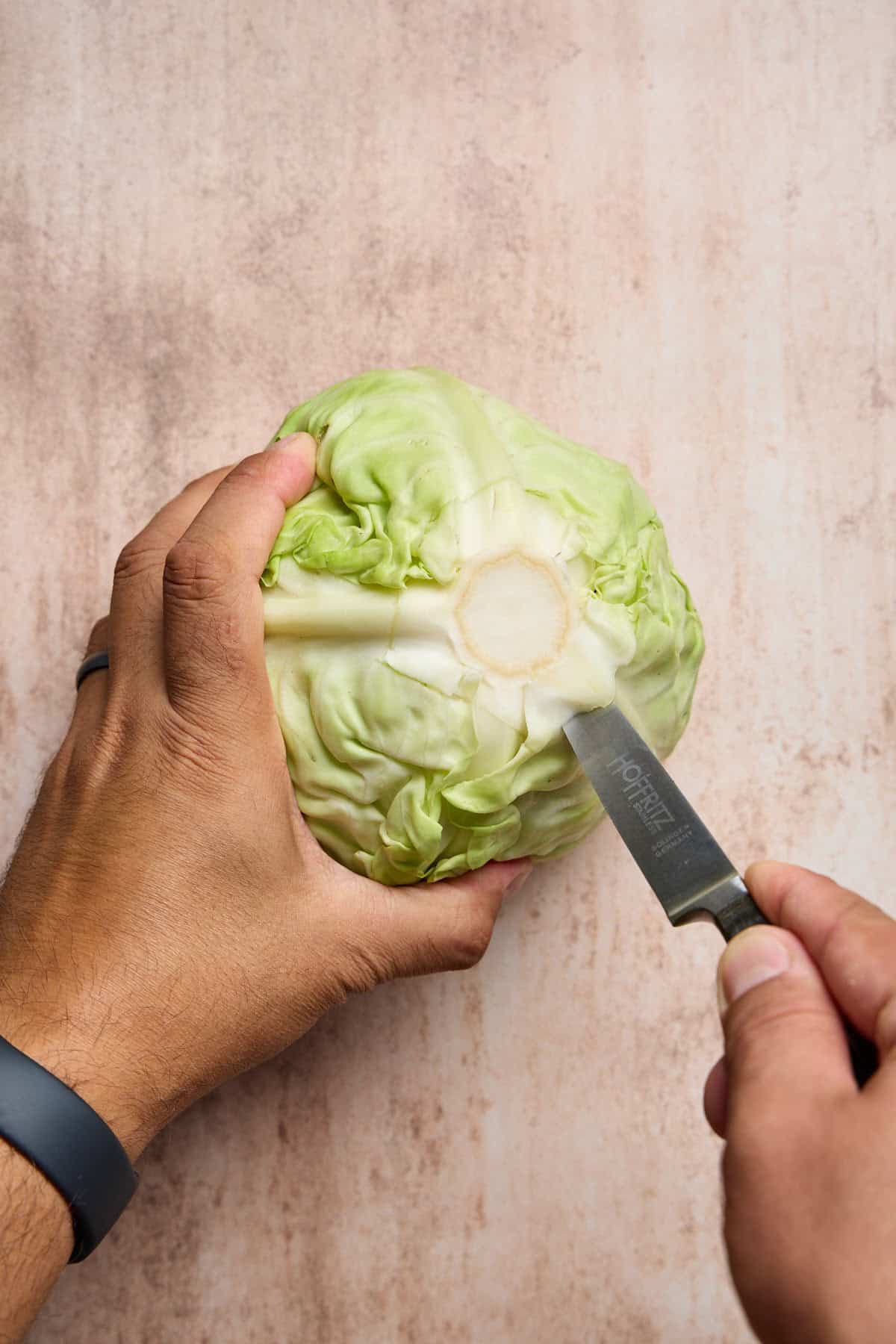 hands holding a cabbage and using a knife to cut out the core