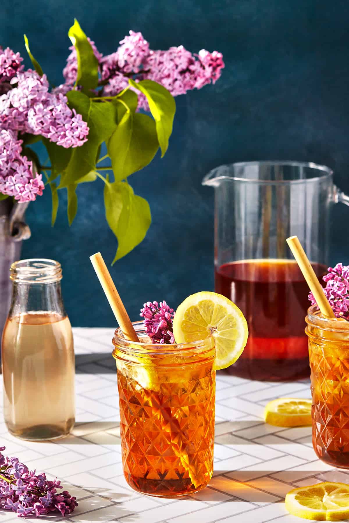 glasses of lilac iced tea with a pitcher and flowers
