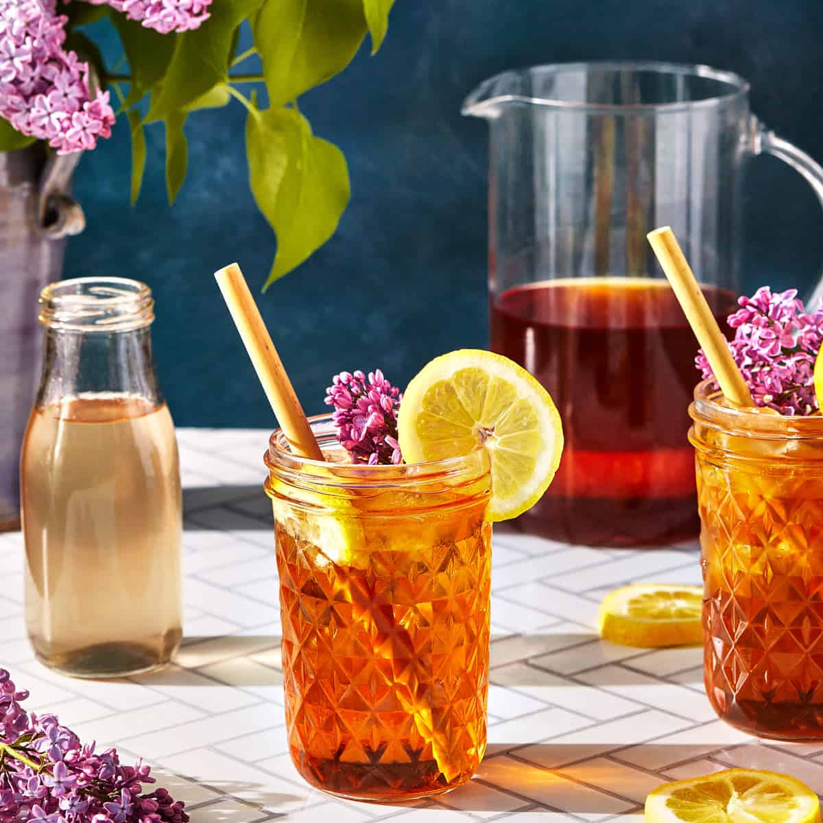 glasses of lilac tea with ice, pitcher, and flowers