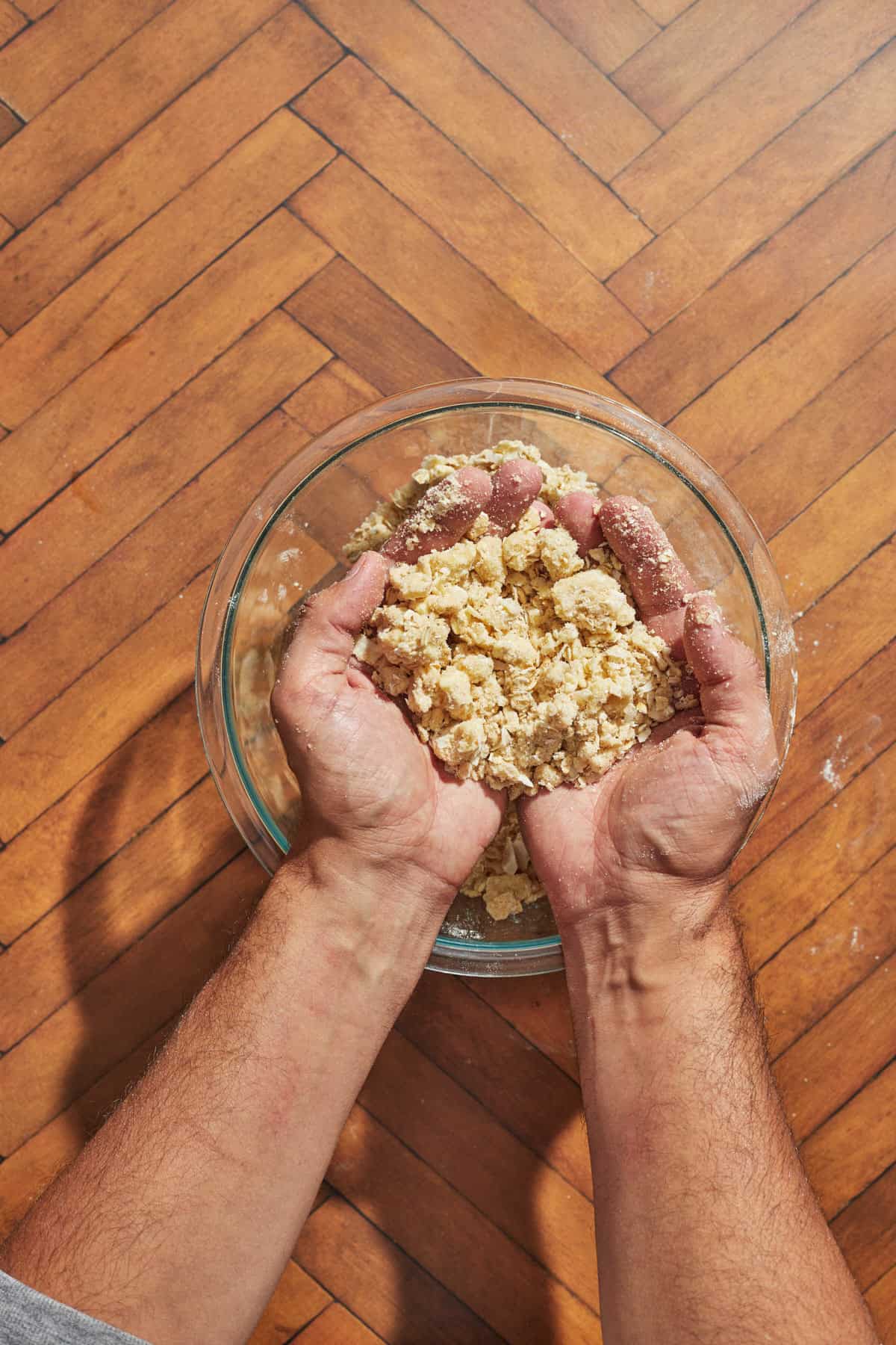 crumble topping in hands over the bowl of mixed ingredients