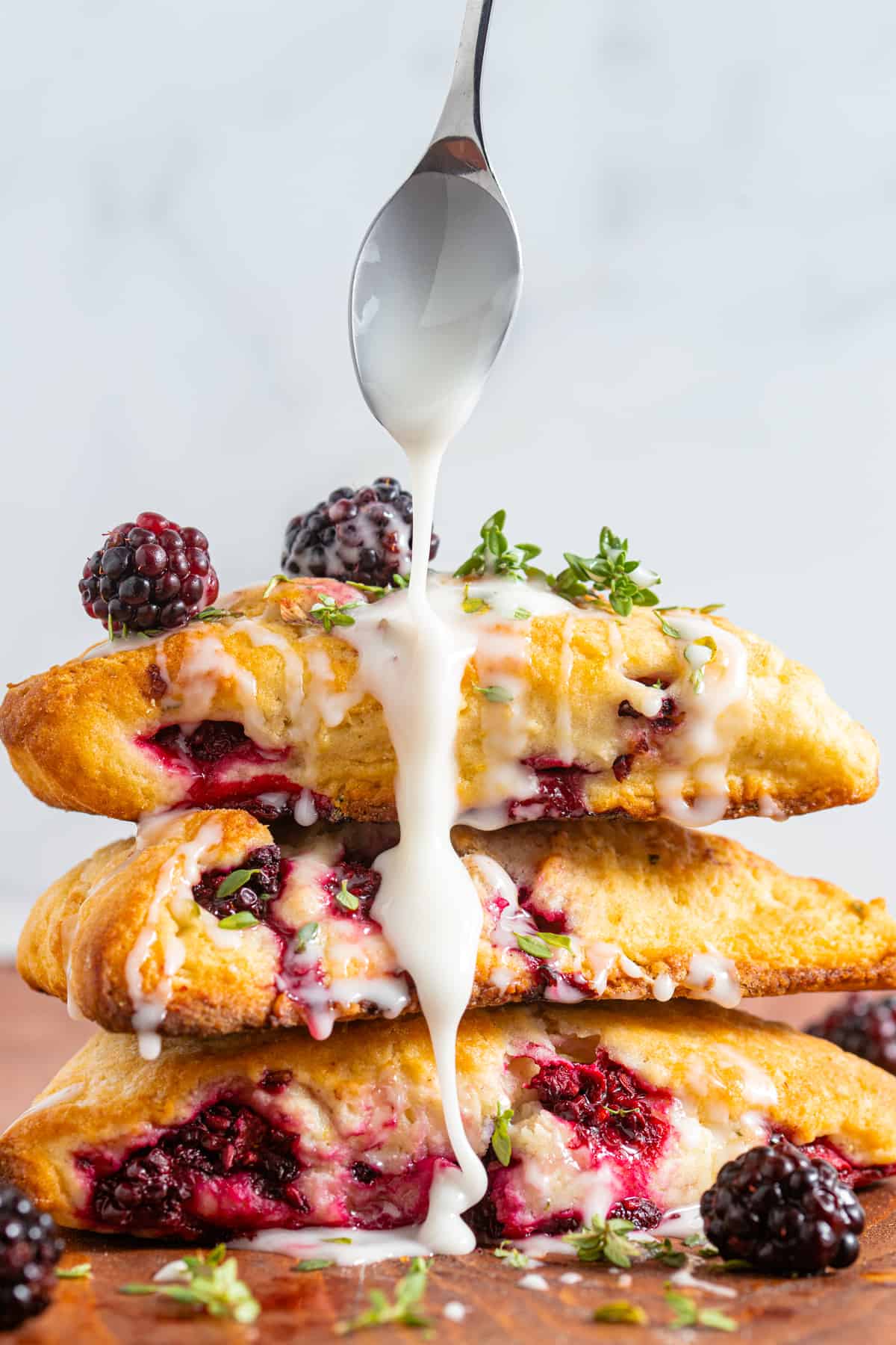 a stack of blackberry scones with a spoon drizzling over lemon glaze