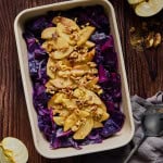a serving dish on a wooden table filled with cabbage, apples, and walnuts