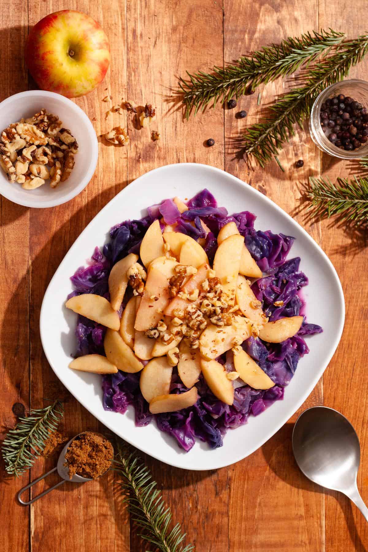 a plate of red cabbage topped with apples and walnuts with ingredients surrounding the plate