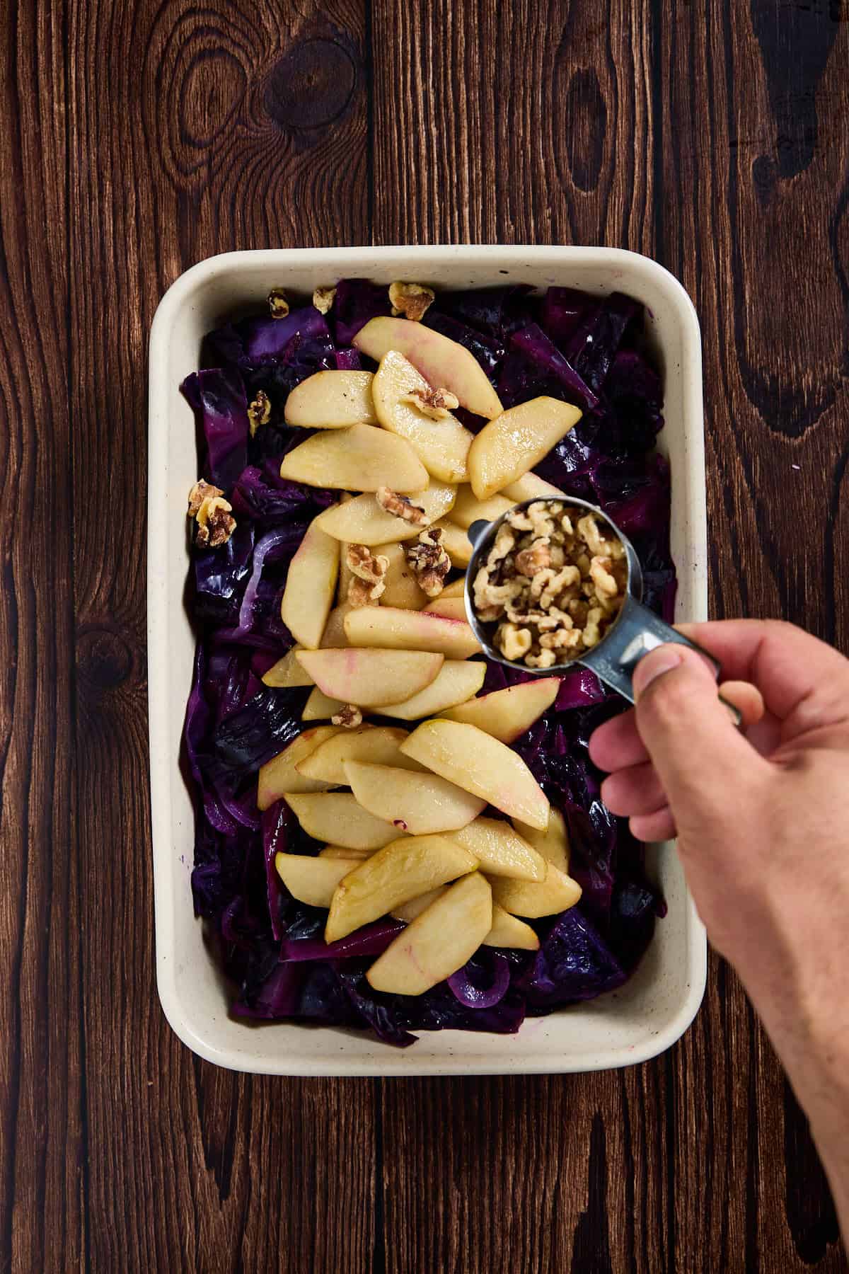 walnuts being poured over a dish of cabbage and apples