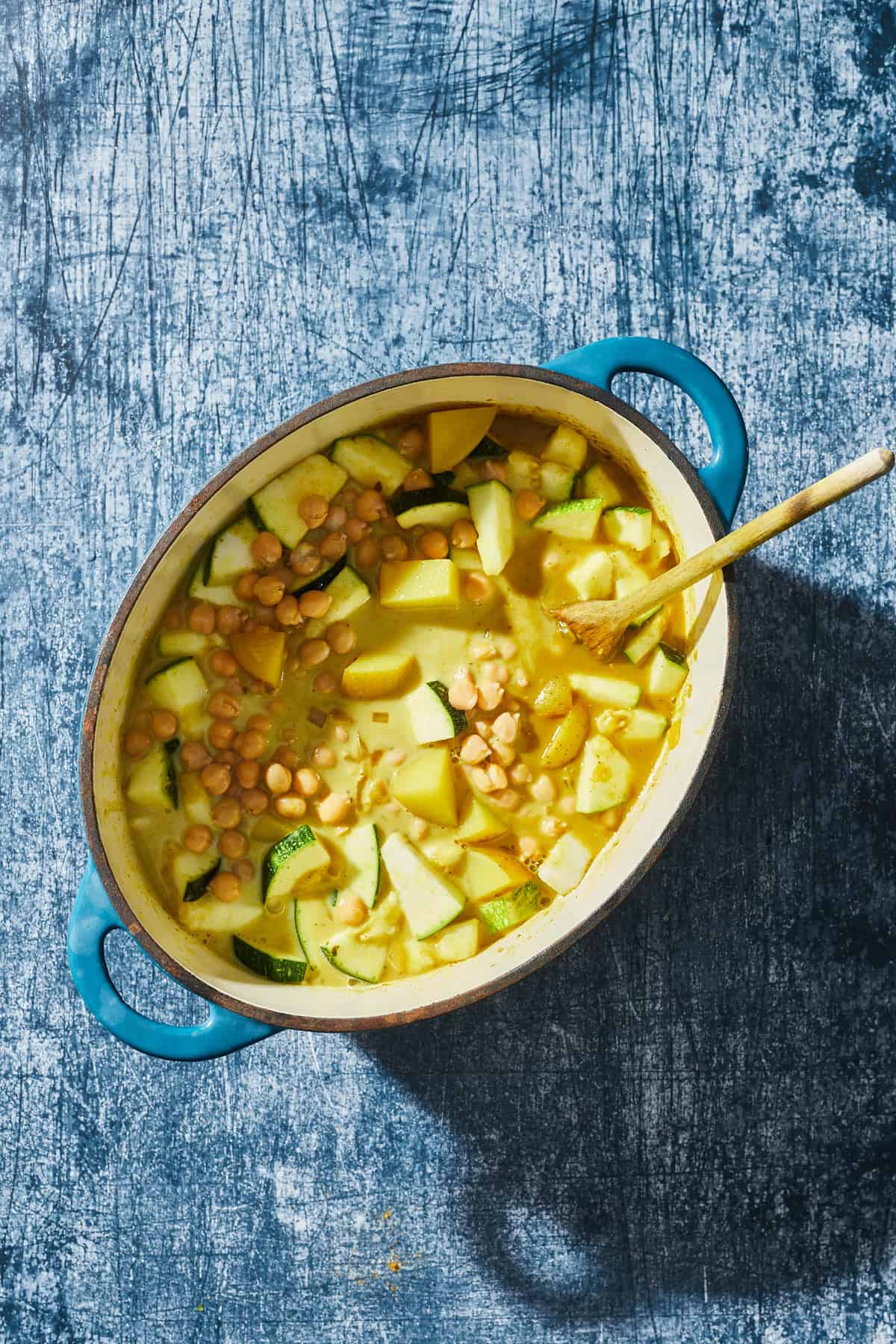 a pot with potatoes, chickpeas, zucchini, and onions cooking in coconut milk and broth