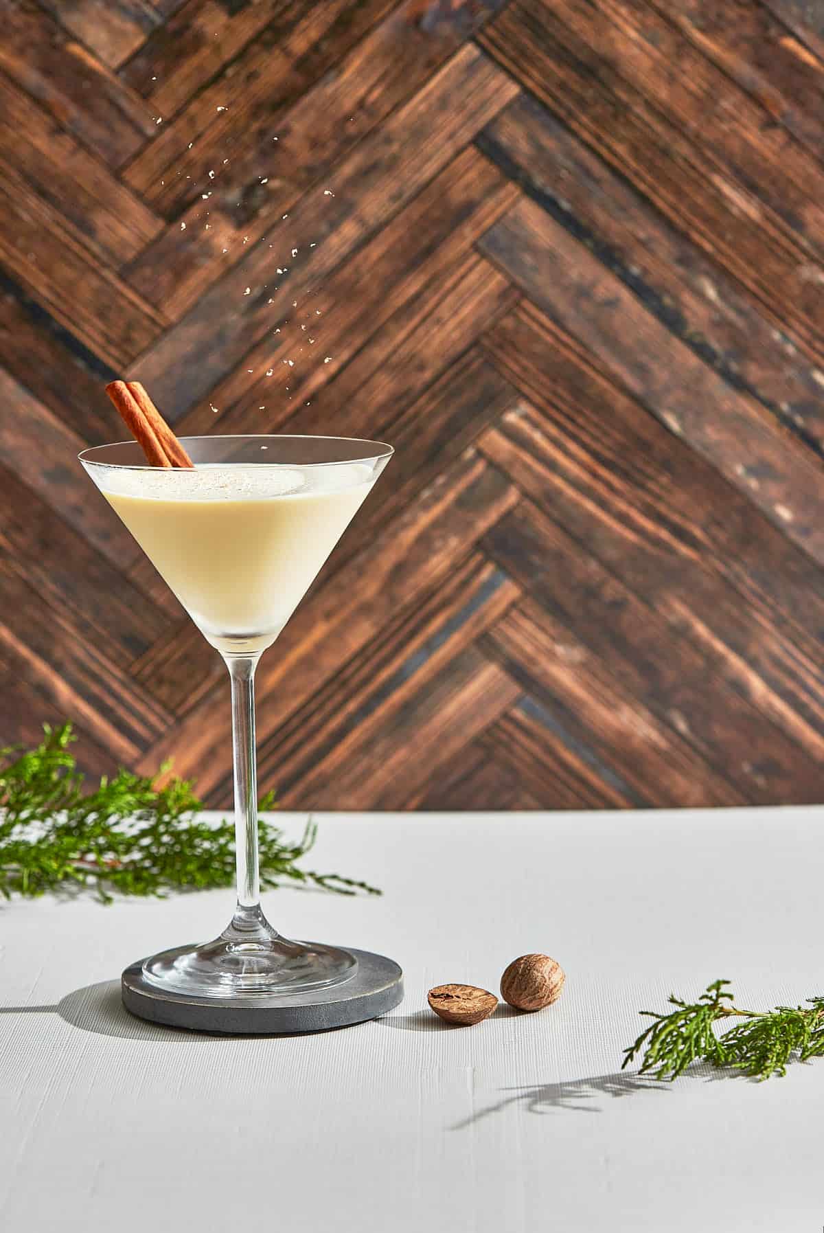 a martini glass filled with an eggnog cocktail and grated nutmeg falling down into the glass
