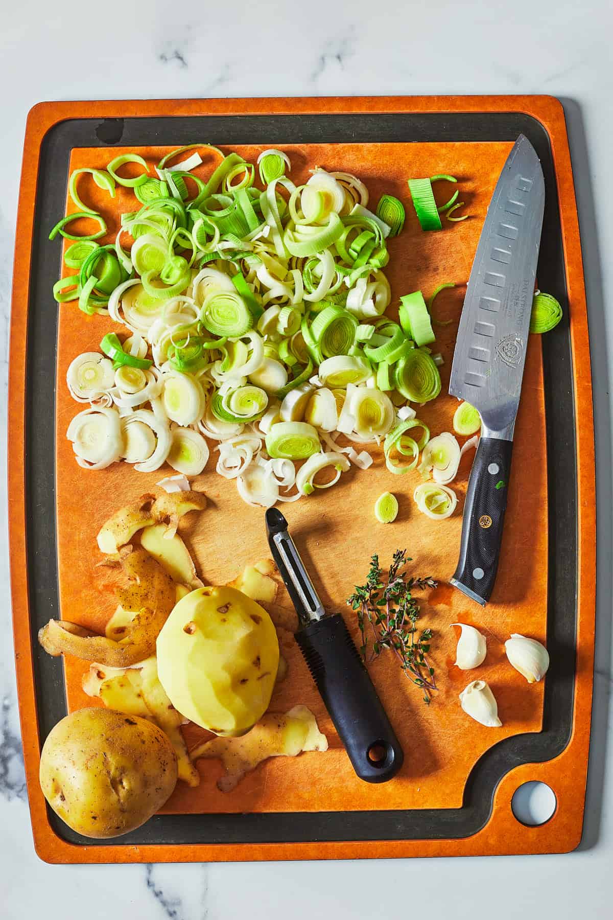 leeks chopped, potatoes being peeled on cutting board with knife and peeler