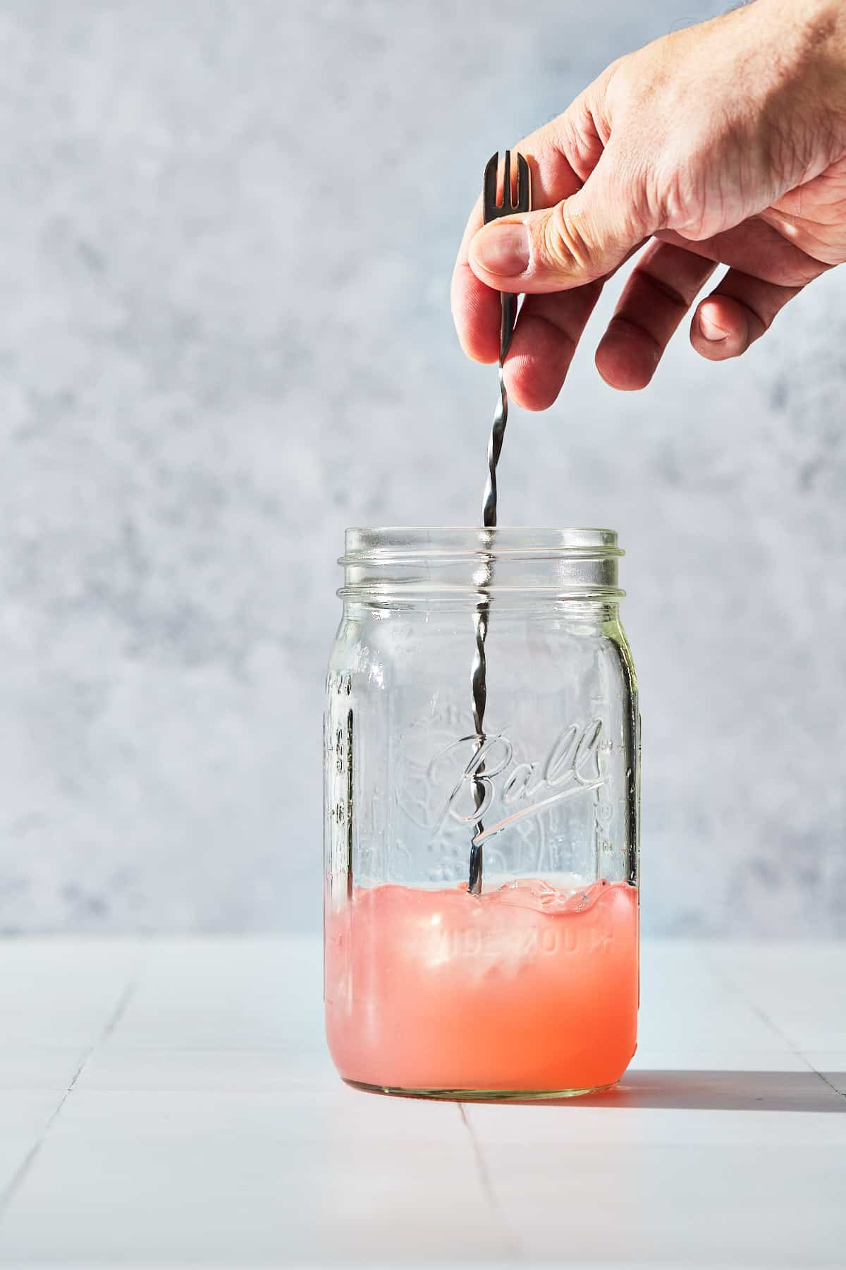 rhubarb gin cocktail being stirred in a large jar with ice