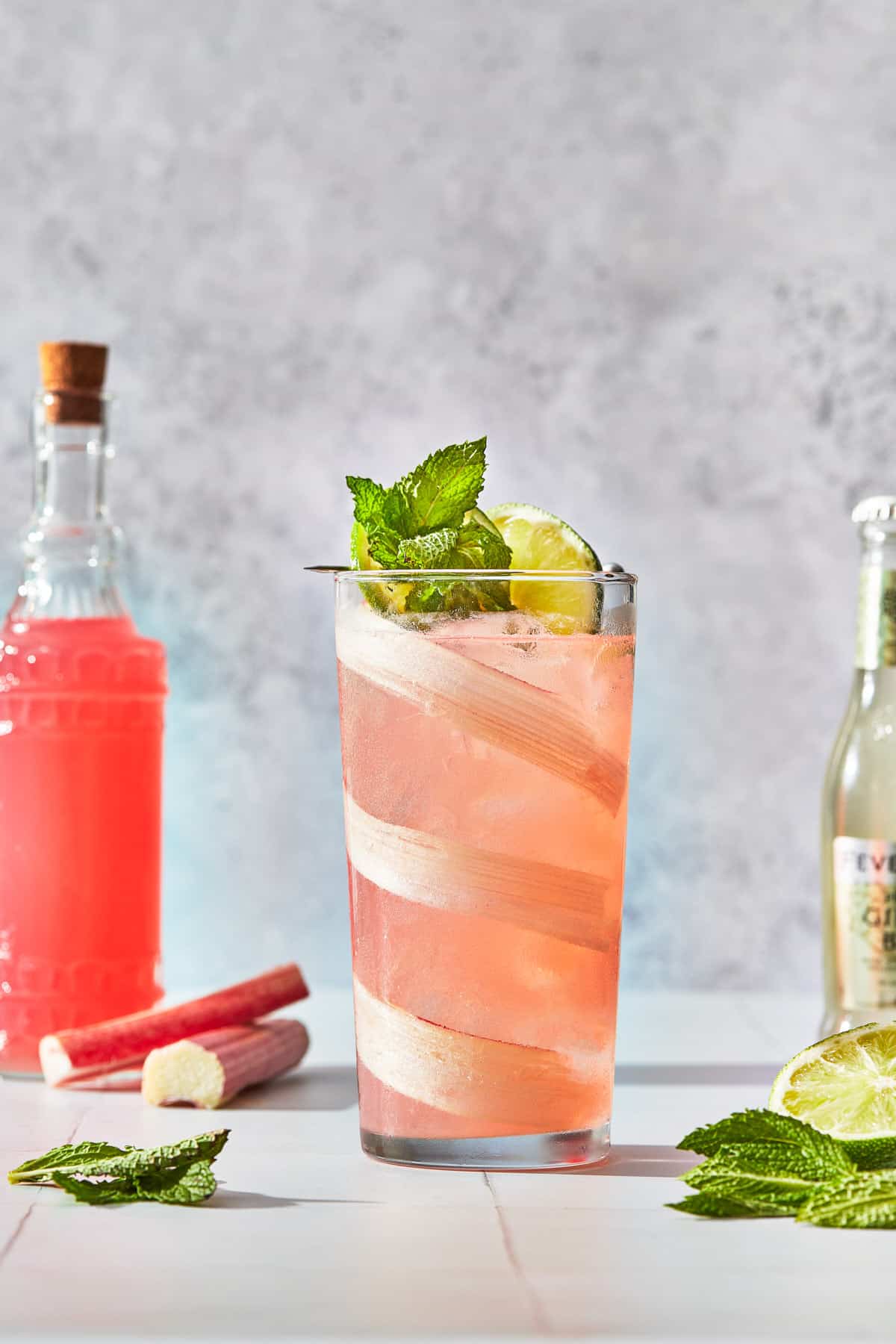 rhubarb ginger gin cocktail in a glass with mint and limes and rhubarb to the side