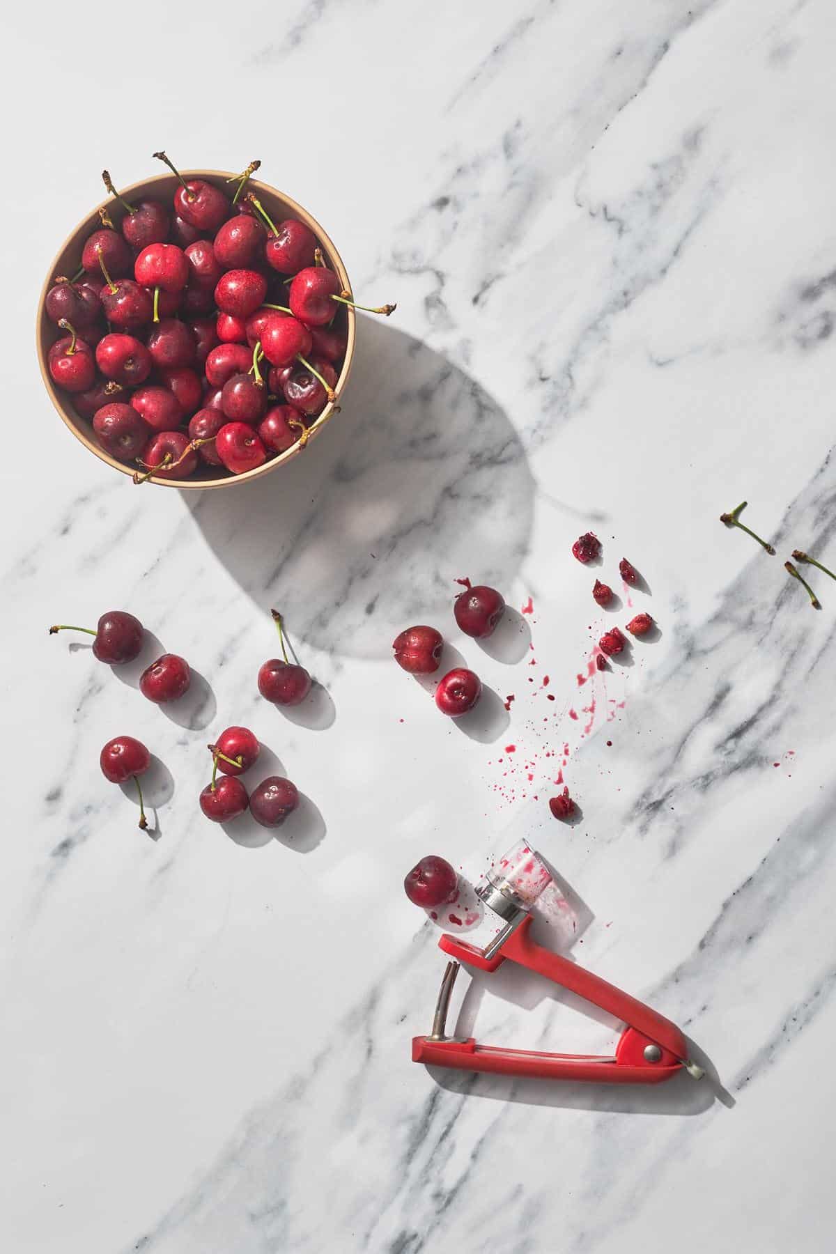 a bowl of cherries and cherry pitter on marble counter