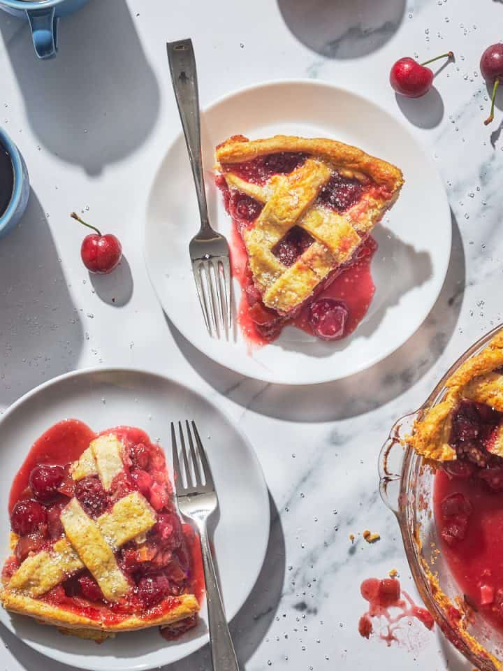two pieces of cherry pie on plates with coffee cups