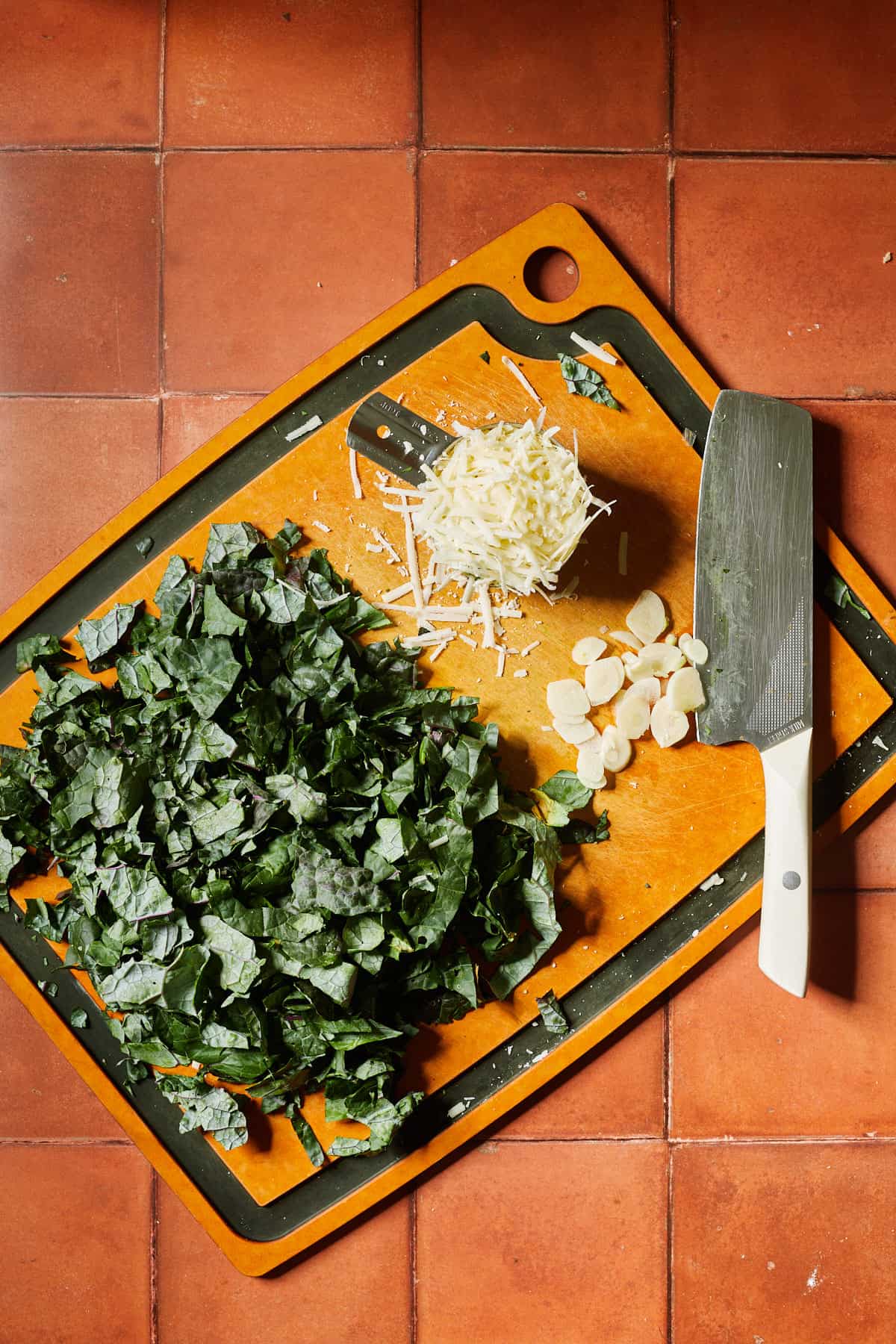 kale, garlic and cheese being prepped on a cutting board with a knife