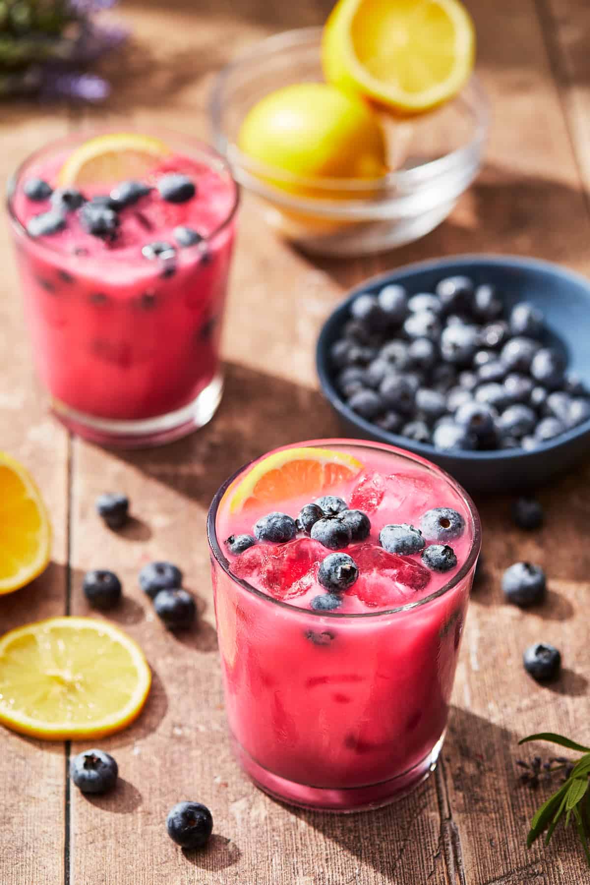 glasses of pink blueberry lemonade with a bowl of blueberries and slices of lemon