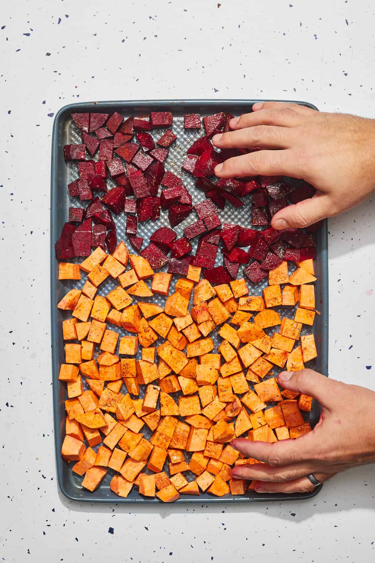 hands tossing sweet potato and beets with spices