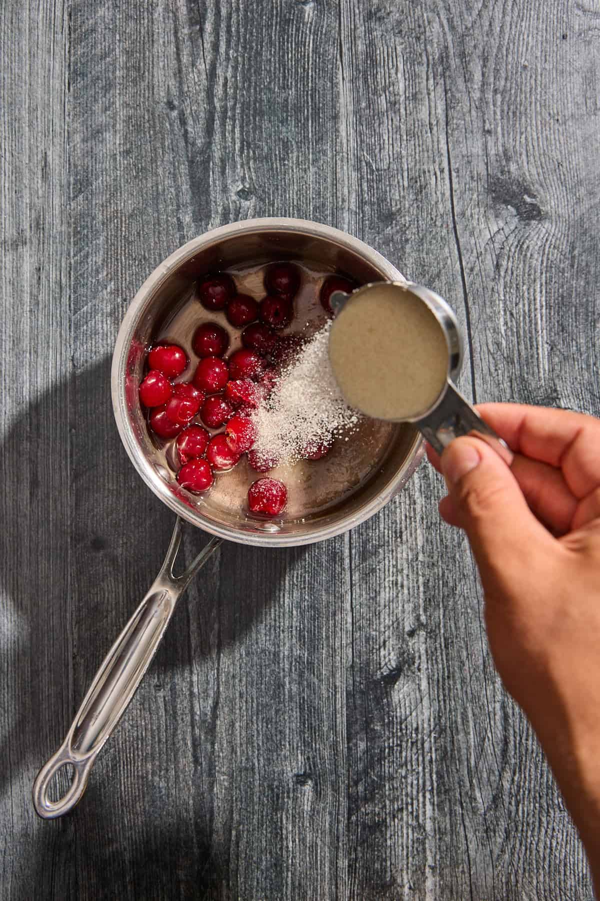 sugar being added to a small pot of cherries