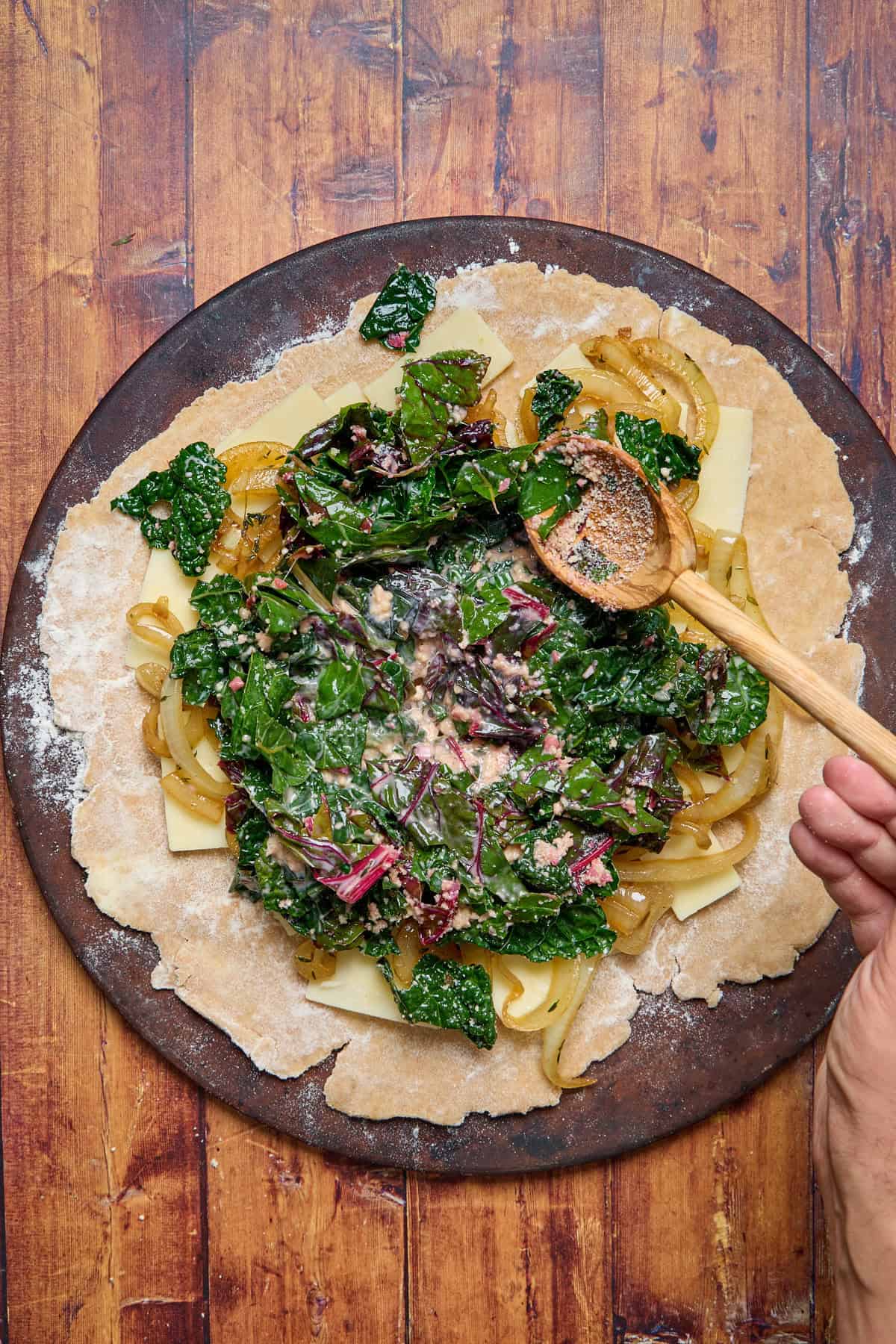 cooked greens being spread over the galette