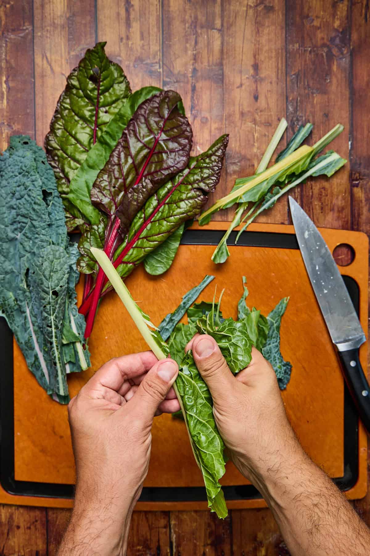 ribs of the kale and swiss chard being removed on cutting board