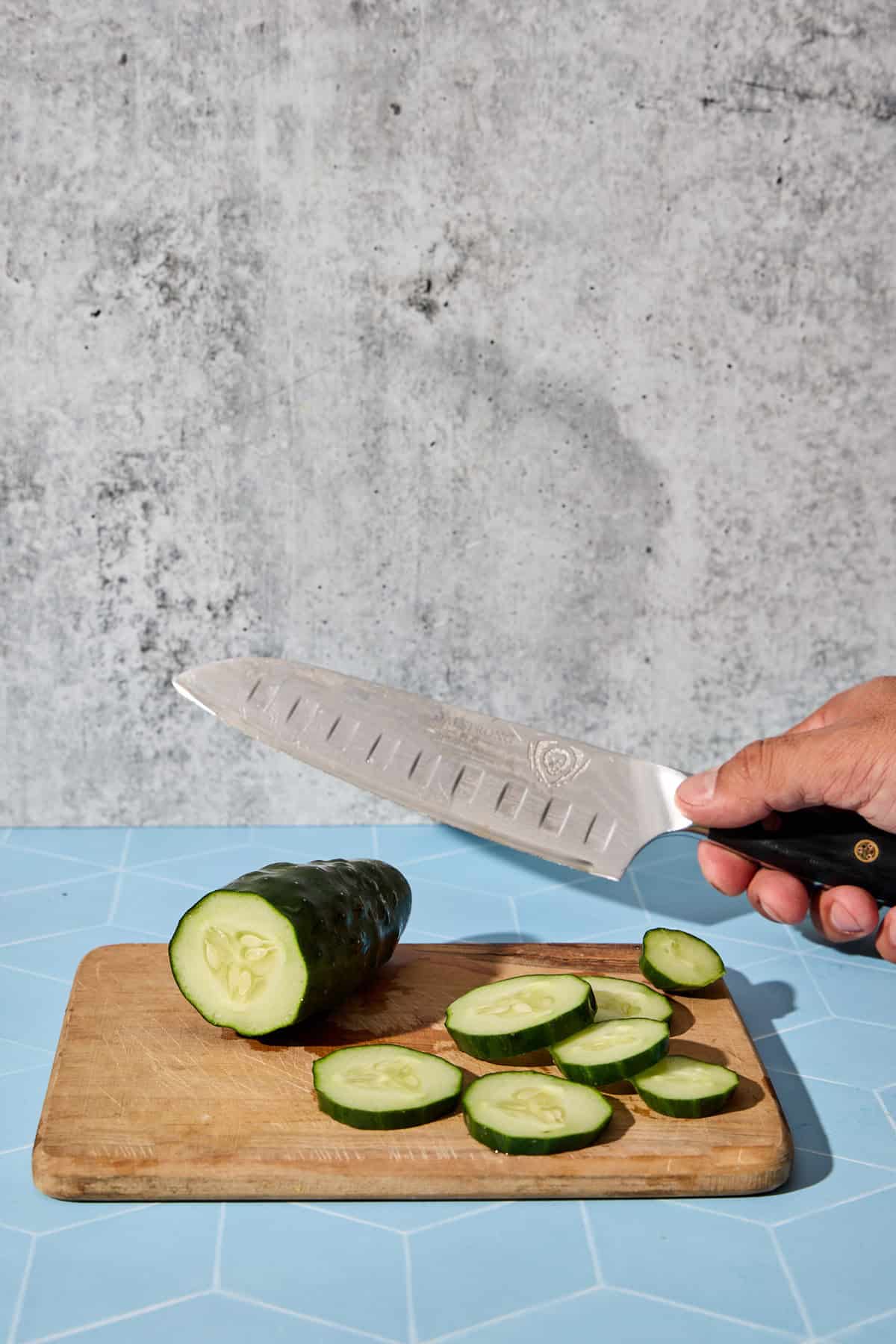 a cucumber on a cutting board being sliced with a knife for the cocktail