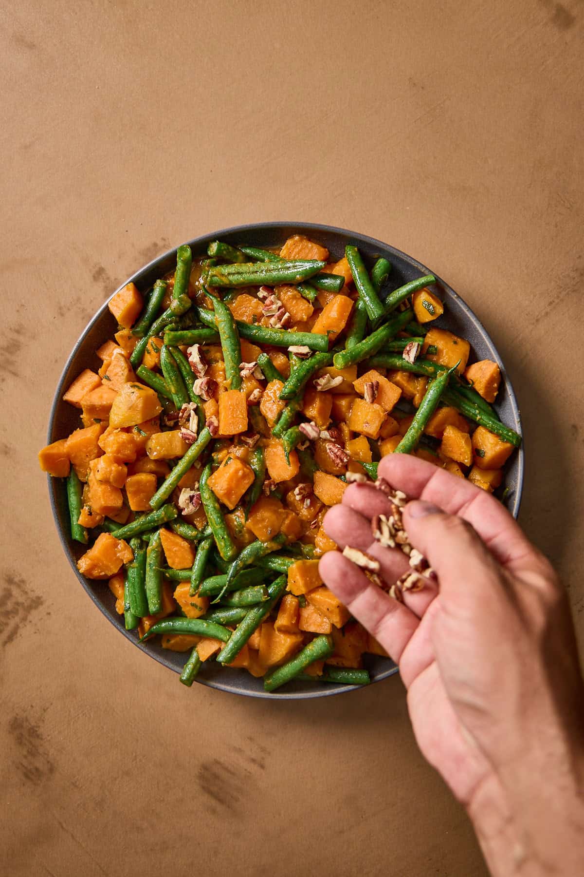 chopped pecans being added to pan with beans and sweet potatoes