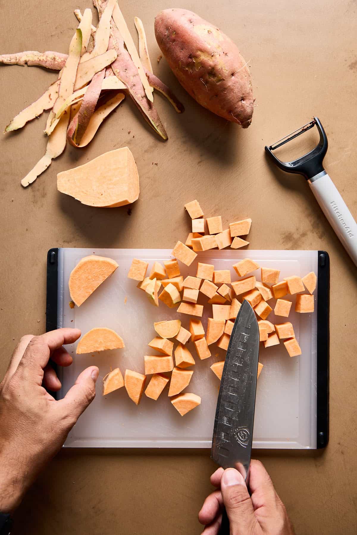 sweet potatoes being peeled and cubed on a cutting board