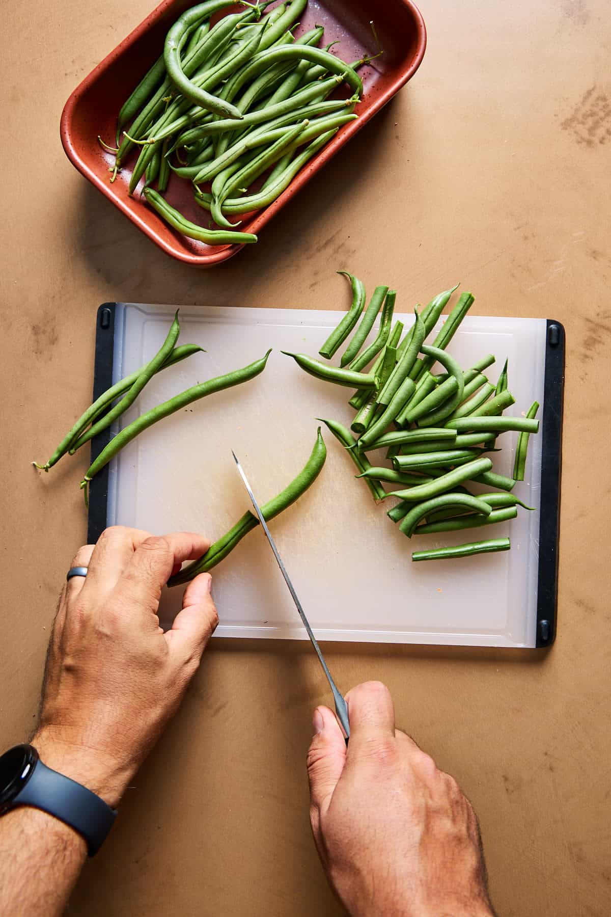 green beans being trimmed on a cutting board