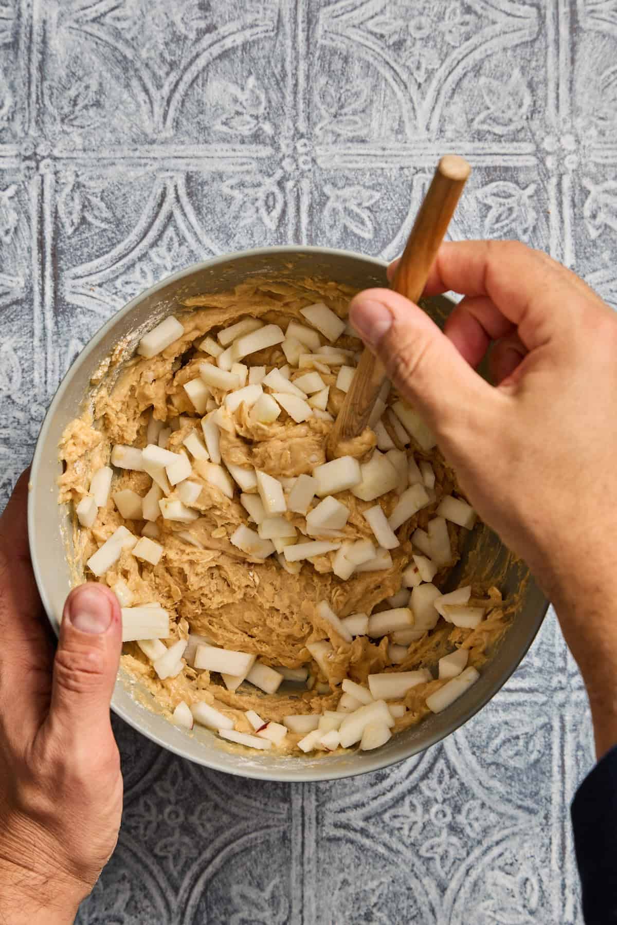 apples being stirred into a bowl of muffin batter