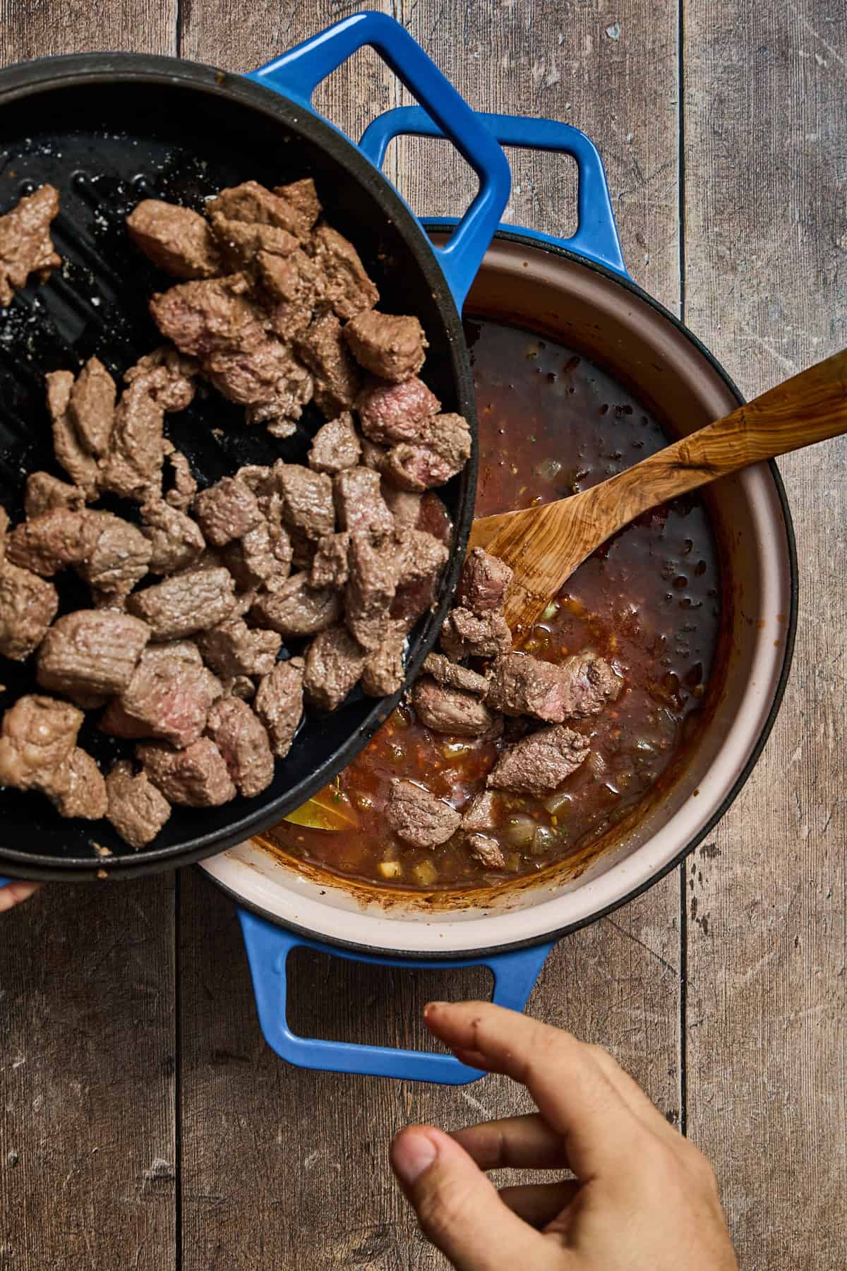 browned beef being added to the pot of stew