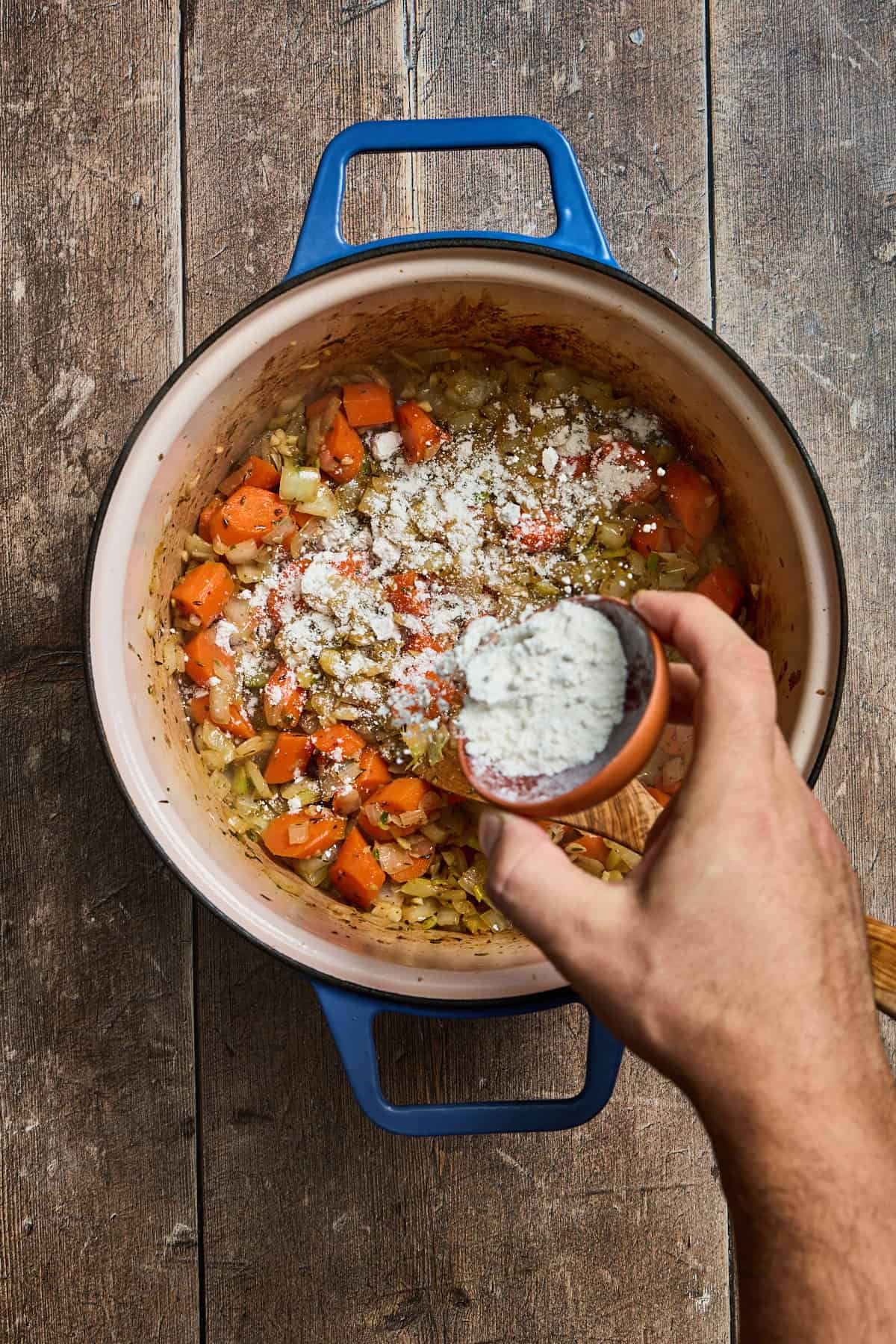 flour being sprinkled over cooked vegetables in a pan