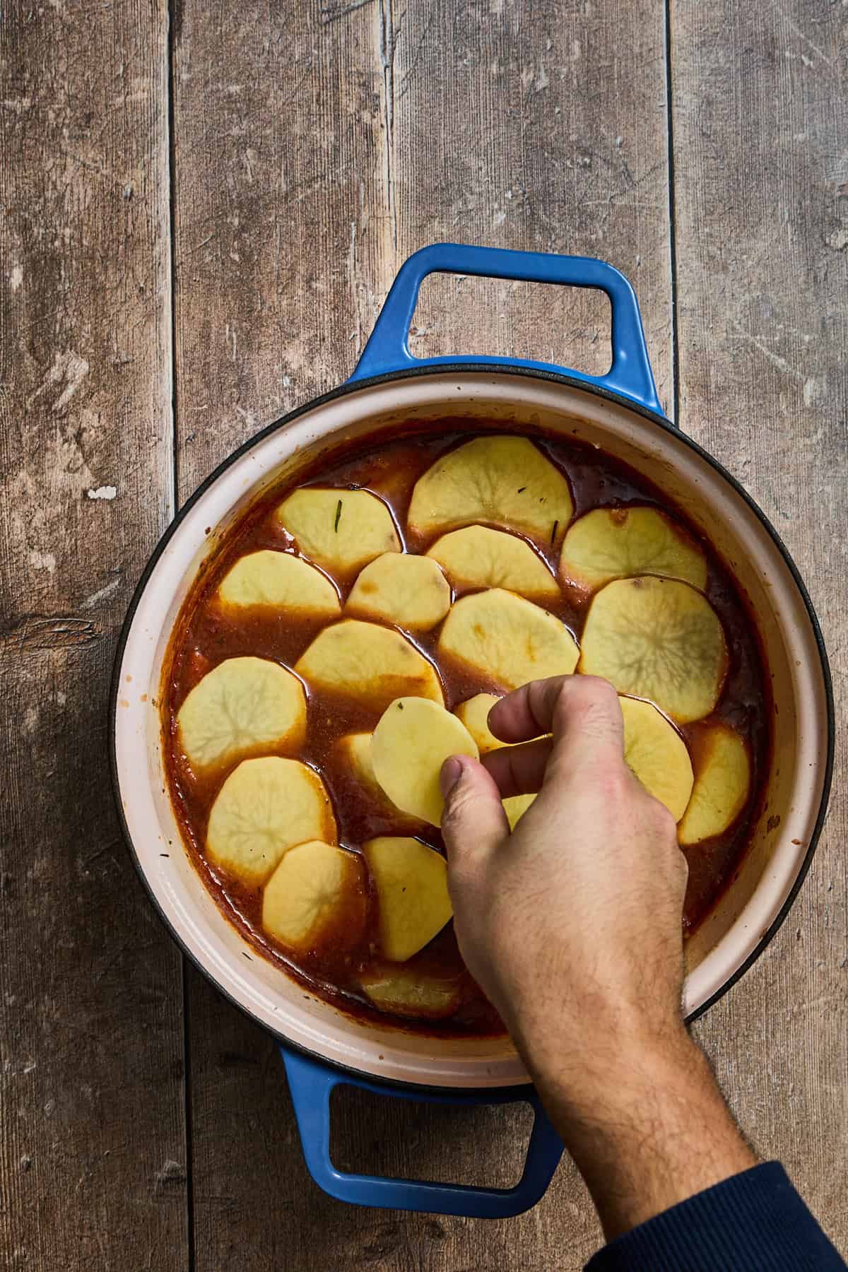 sliced potatoes being layered over the lancashire hotpot