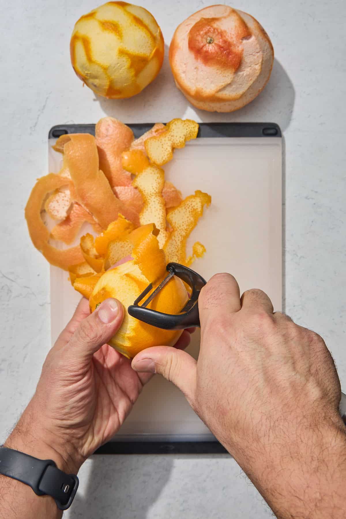 an orange being peeled over a cutting board