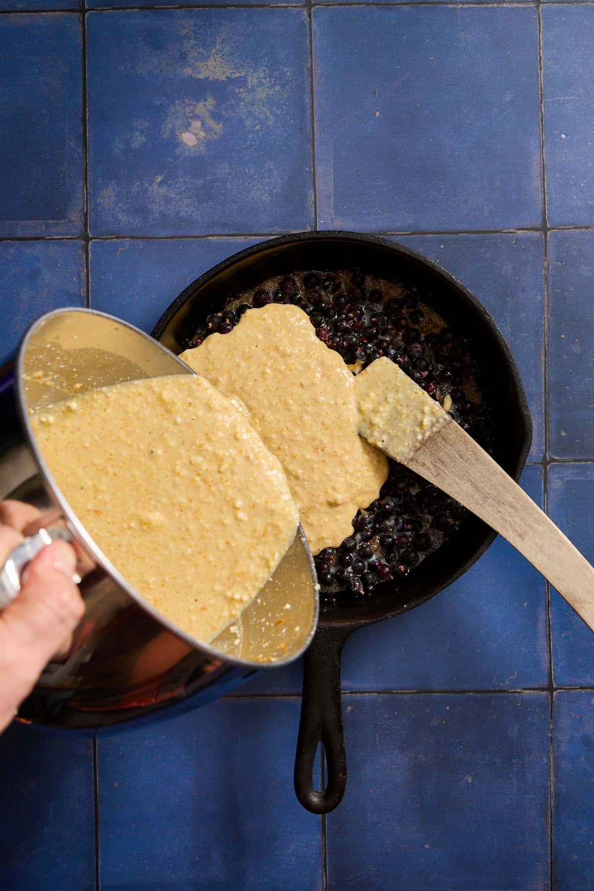 cake batter being poured over a pan of blackcurrants and caramel