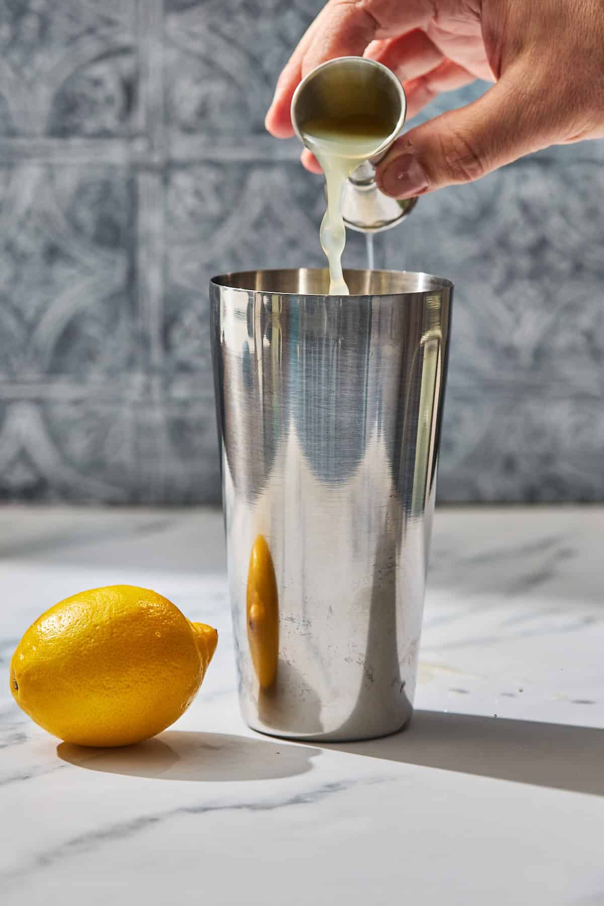 lemon juice being poured into a cocktail shaker