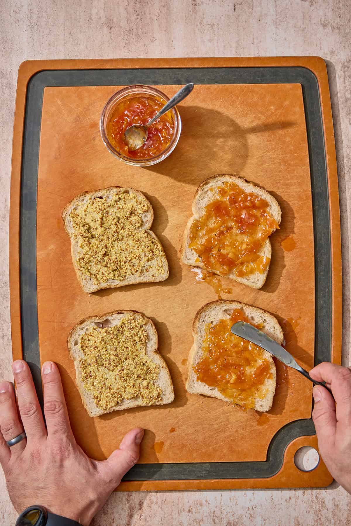 mustard and marmalade being spread on slices of bread on a cutting board