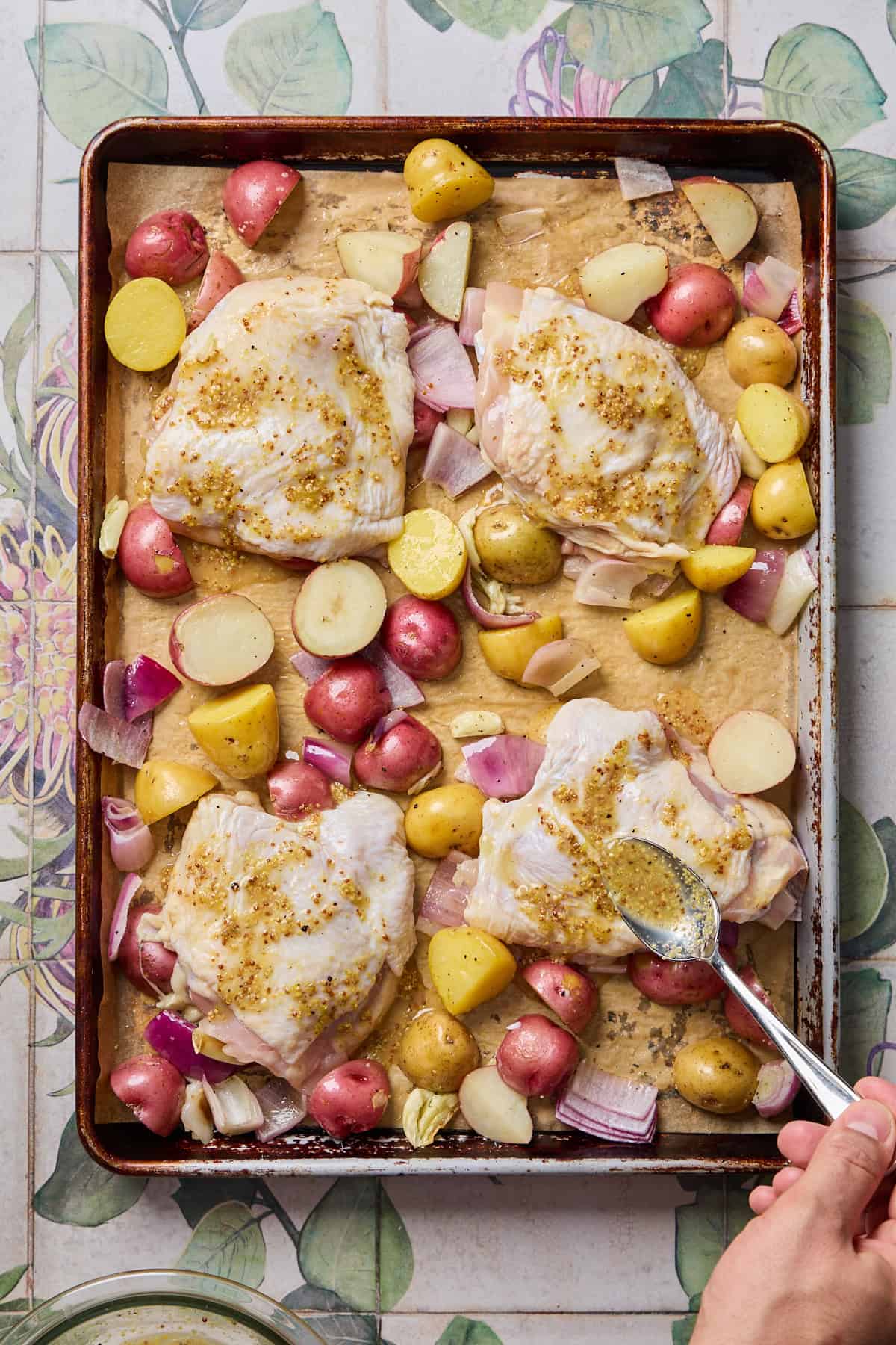 chicken on a tray with potatoes and onions with sauce being spooned over