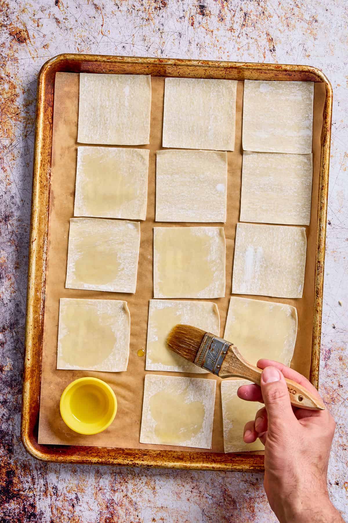 wonton wrappers on a tray being brushed with oil