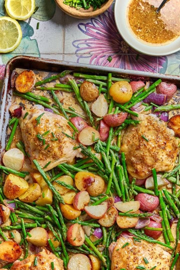 a tray of roasted chicken with asparagus, potatoes, and lemons