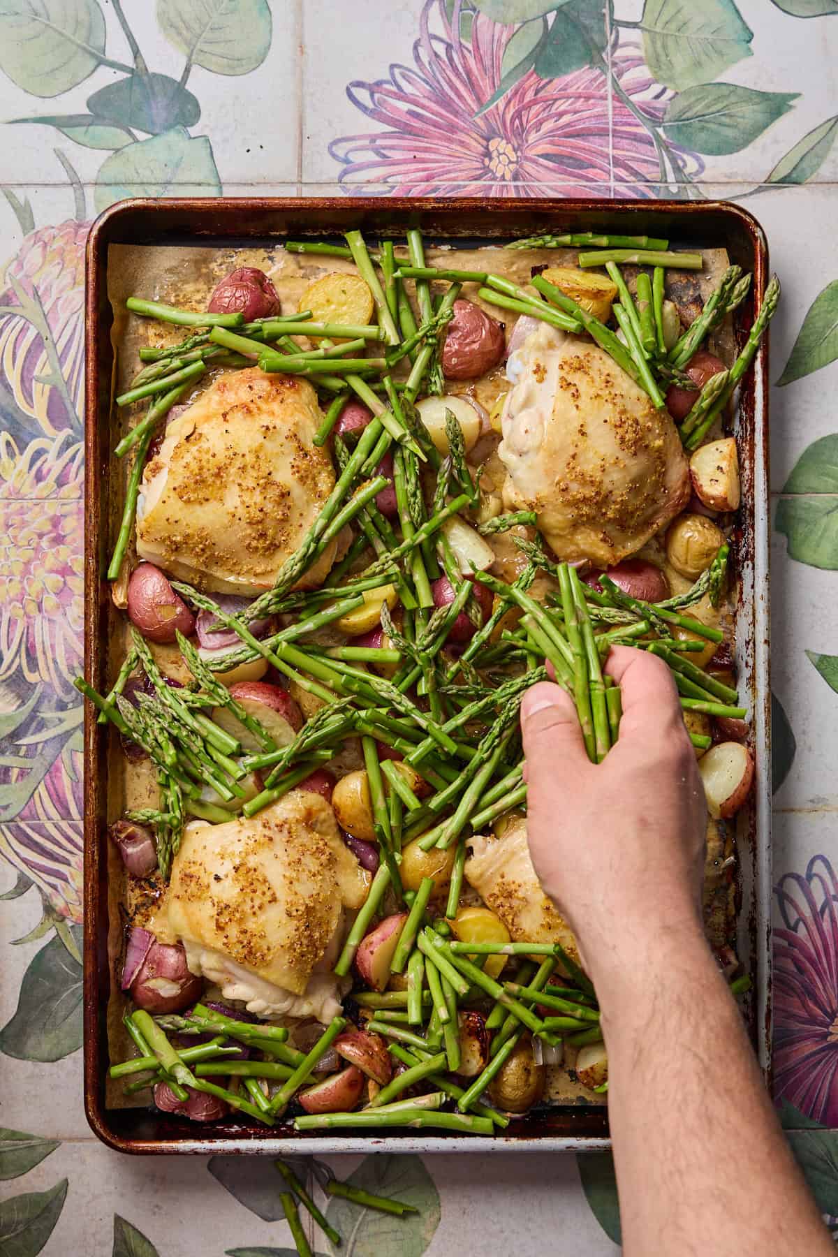 asparagus being added to the roasting tray with chicken and potatoes on it