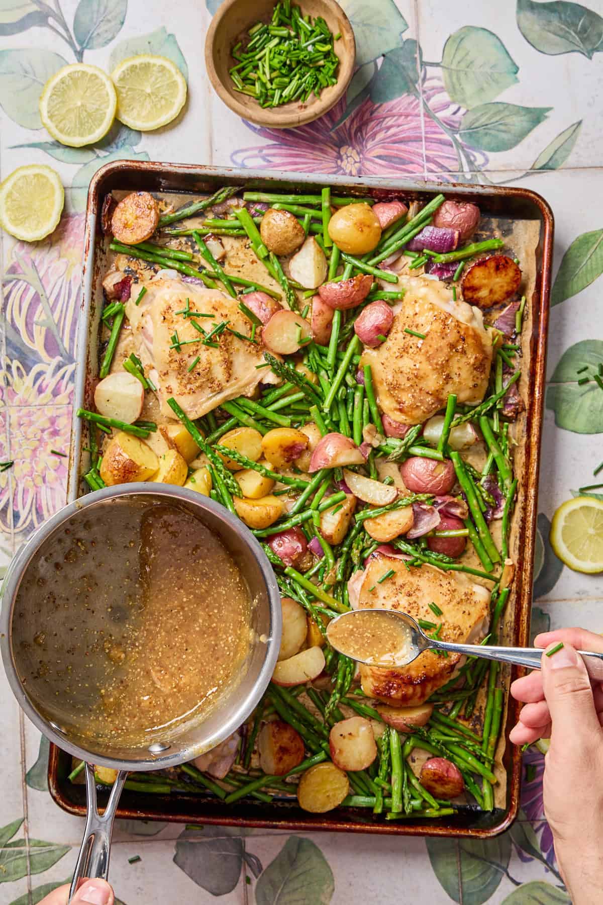 lemon sauce being spooned over the tray of cooked chicken and vegetables