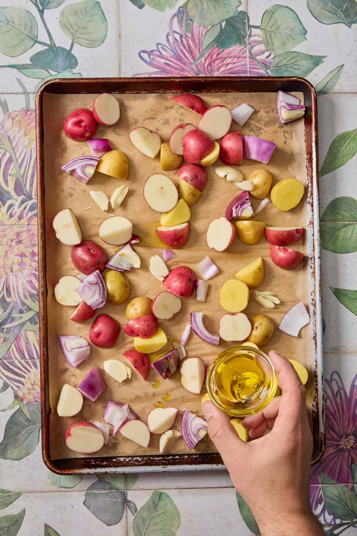 onions and potatoes on a roasting tray with oil being poured over them