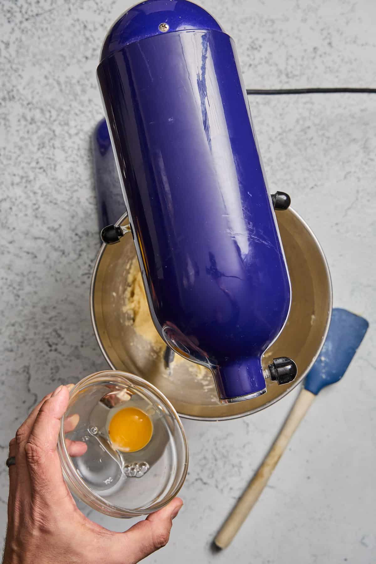 eggs being added to a bowl of stand mixer